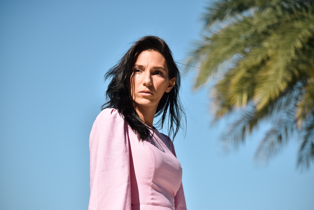 a woman in a pink dress standing next to a palm tree
