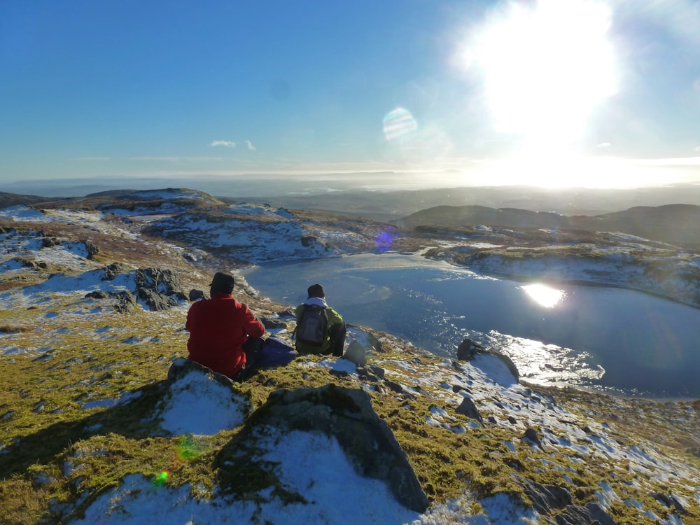 a couple of people sitting on top of a snow covered hill