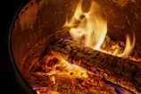 Copper smoker door open with glowing embers inside, surrounded by wood logs and smoke.