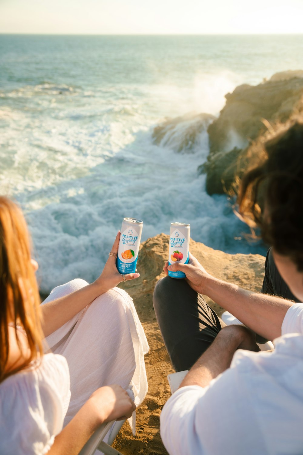 a man and a woman sitting on a cliff by the ocean