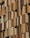 A facade of a building featuring numerous vertical panels in varying shades of brown and beige, arranged in an overlapping pattern. The panels have a perforated texture, allowing glimpse of the windows behind them.