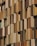 A facade of a building featuring numerous vertical panels in varying shades of brown and beige, arranged in an overlapping pattern. The panels have a perforated texture, allowing glimpse of the windows behind them.