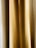 A close-up view of golden beige curtains with soft, vertical folds. The texture appears smooth, and the light creates subtle gradients.
