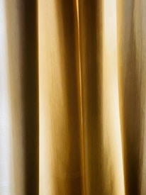 A close-up view of golden beige curtains with soft, vertical folds. The texture appears smooth, and the light creates subtle gradients.