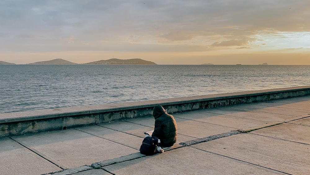 a man sitting on the edge of a pier next to the ocean