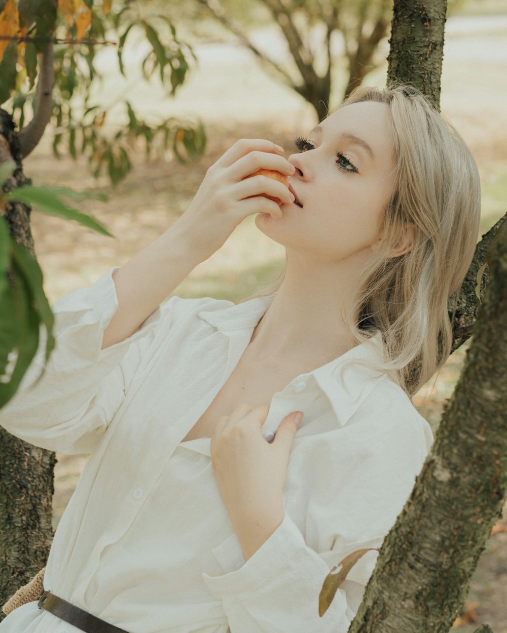 a woman in a white shirt leaning against a tree