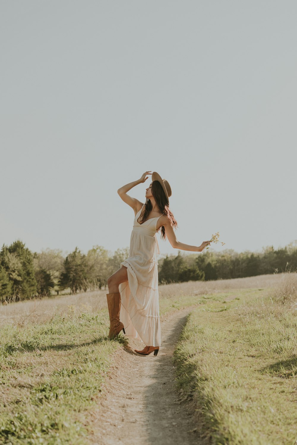 Eine Frau in weißem Kleid und Cowboyhut tanzt auf einem Feldweg