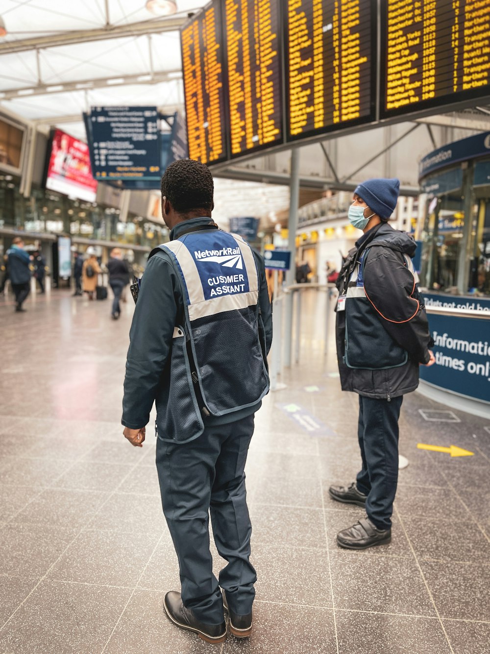 two people standing in an airport waiting for their luggage