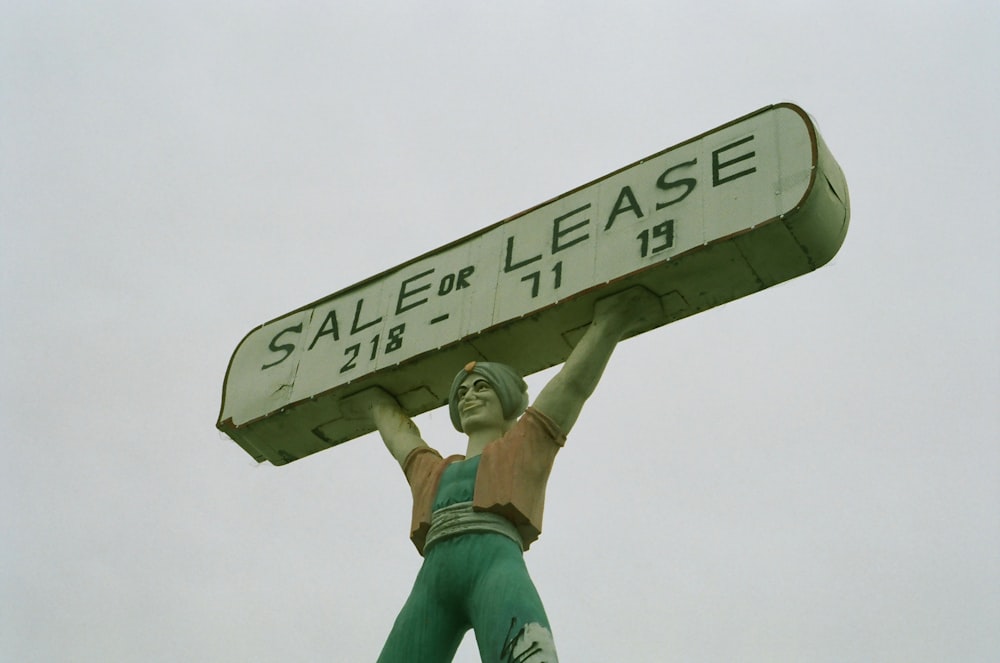 a statue of a man holding a sign that says sale or leases