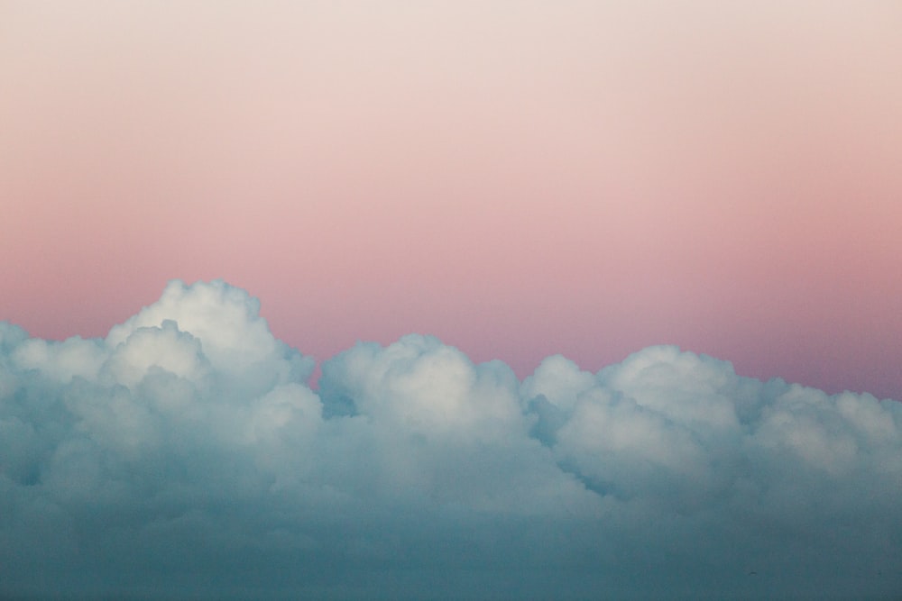 a plane flying through a pink sky with clouds