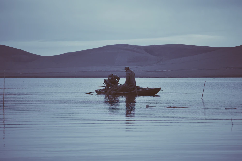 Two people fishing from a small boat on a calm lake