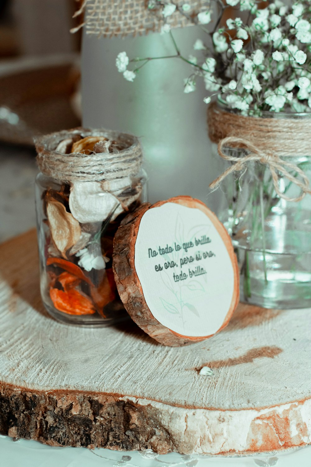 a jar filled with rocks and flowers next to a wooden slice