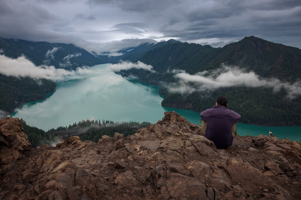 a man sitting on top of a mountain overlooking a lake