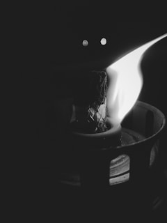 An artistic black and white photo of a lit candle flickering against a dark background