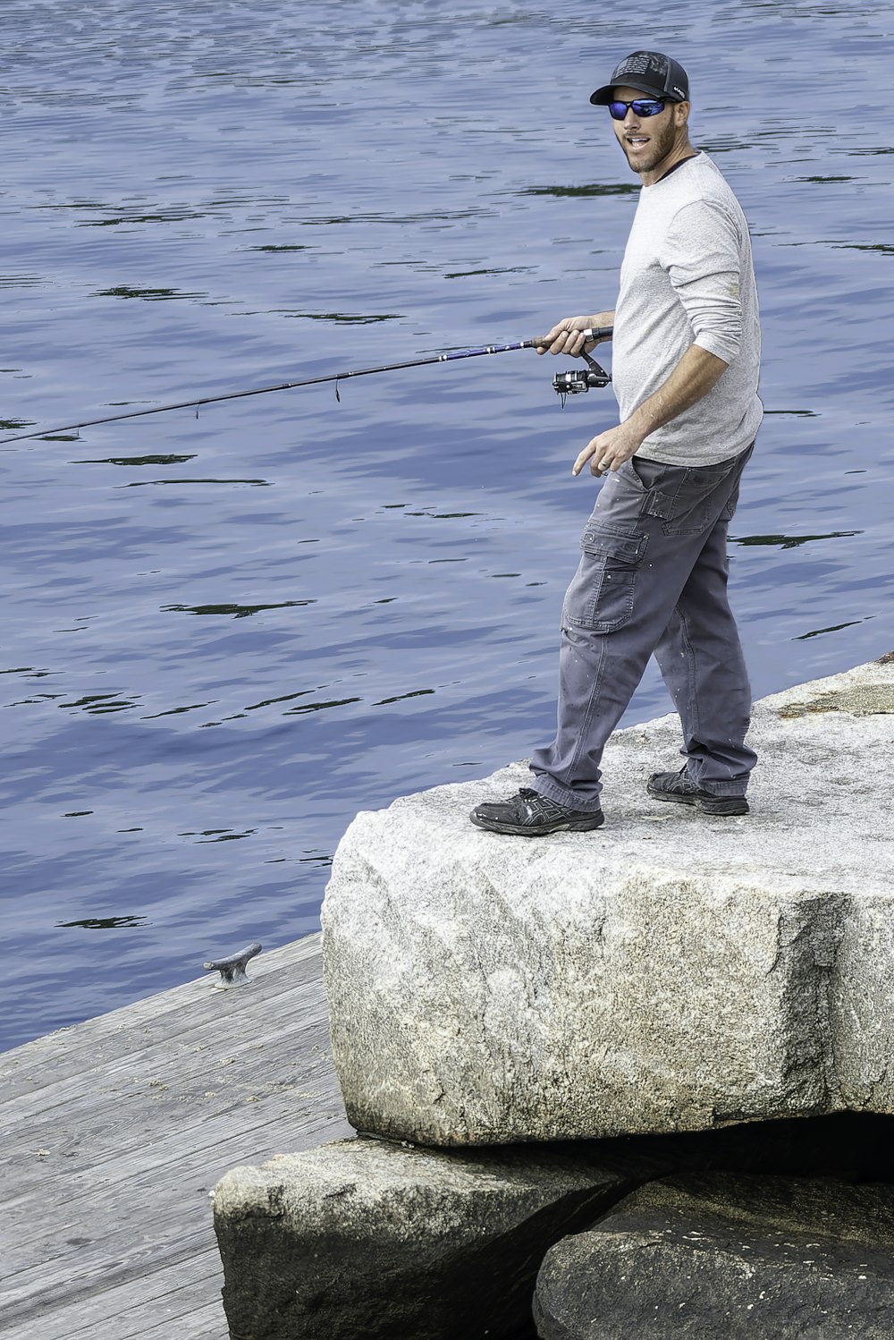 um homem de pé em cima de uma rocha ao lado de um corpo de água