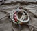 A set of beaded bracelets with multicolored spherical beads interspersed with larger, silver bead accents and tassel embellishments arranged on a textured, brown paper background. The beads include white marbled patterns and various solid colors such as red, yellow, green, and blue.