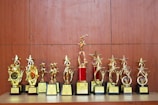 A collection of golden trophies with star designs displayed on a wooden surface. The trophies have various bases, some featuring red accents, and they appear to be awards given for special achievements.