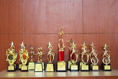A collection of golden trophies with star designs displayed on a wooden surface. The trophies have various bases, some featuring red accents, and they appear to be awards given for special achievements.