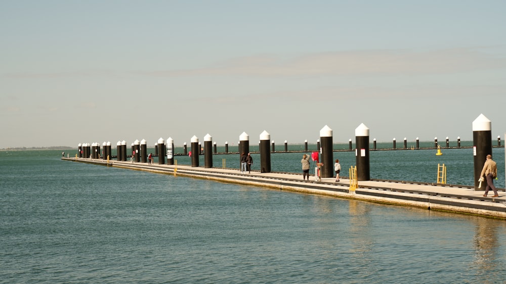 a group of people walking along a pier next to the ocean