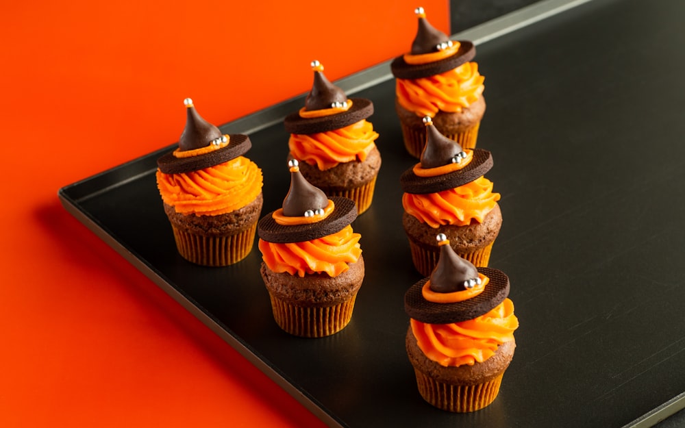 uma bandeja de cupcakes com cobertura de laranja e decorações de chocolate
