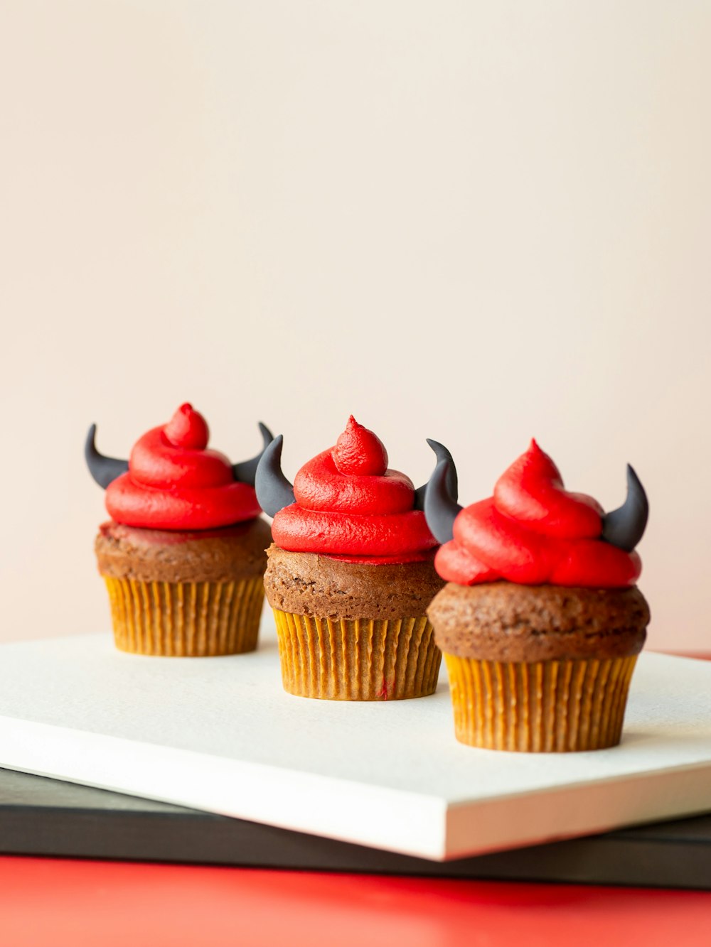 three cupcakes with red frosting and horns on top