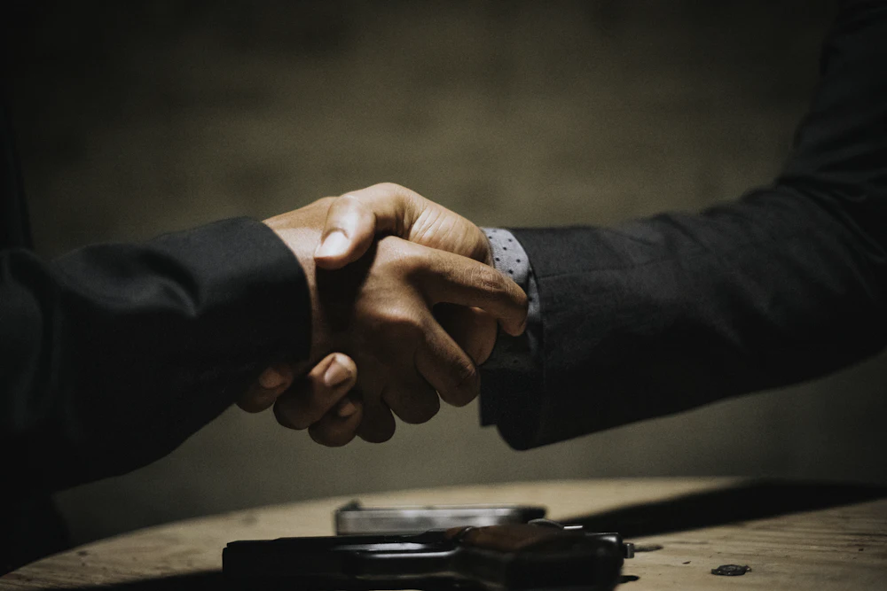 Two people shaking hands across a wooden table after signing an agreement.