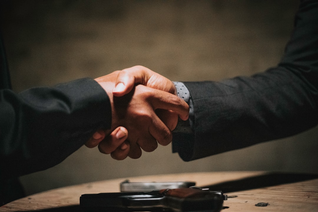 A new client and an account manager shaking hands across a wooden table at a kickoff meeting