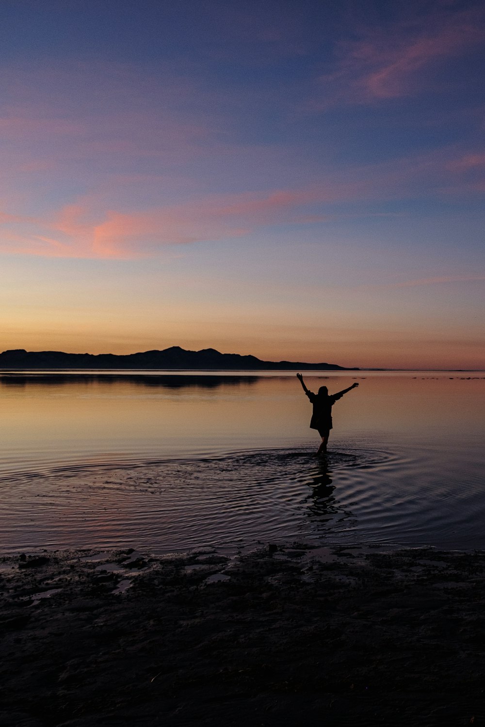 a person standing in a body of water at sunset