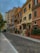 A street lined with colorful, historic buildings featuring architectural details such as shutters, balconies, and decorative molding. The sky is overcast, and the street is empty, providing a peaceful atmosphere.