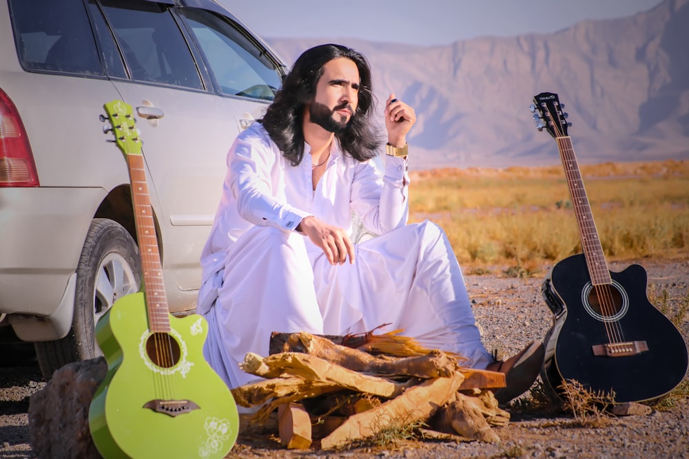 a man sitting on the ground next to a guitar