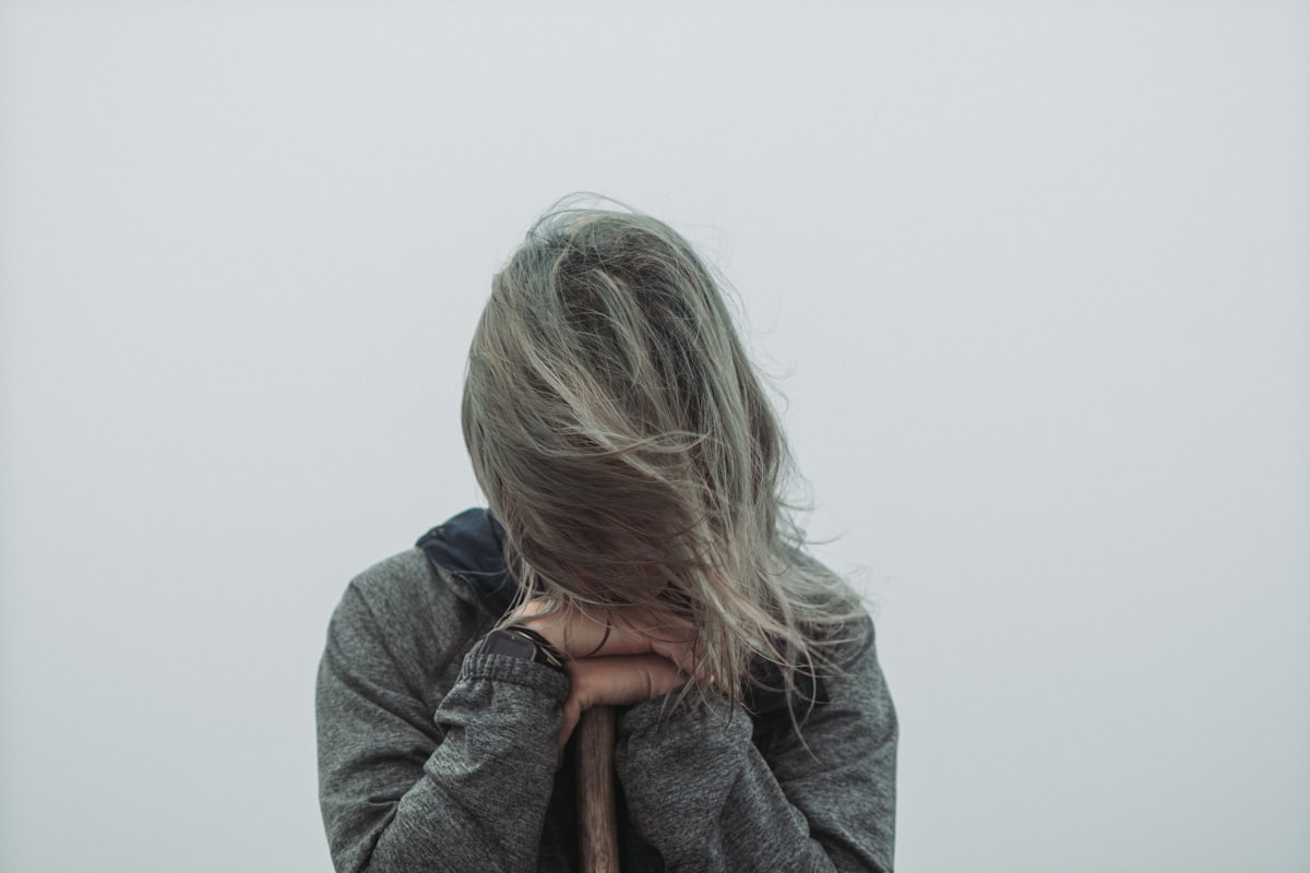 A faceless figure with windswept grey hair resting against a staff under a pale misty sky, second-half-of-life register