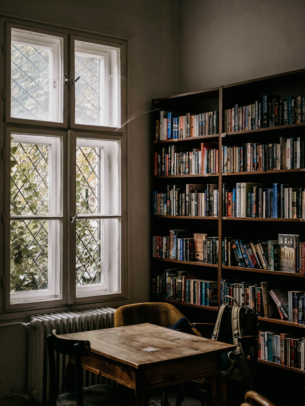 une table en bois assise devant une fenêtre remplie de livres