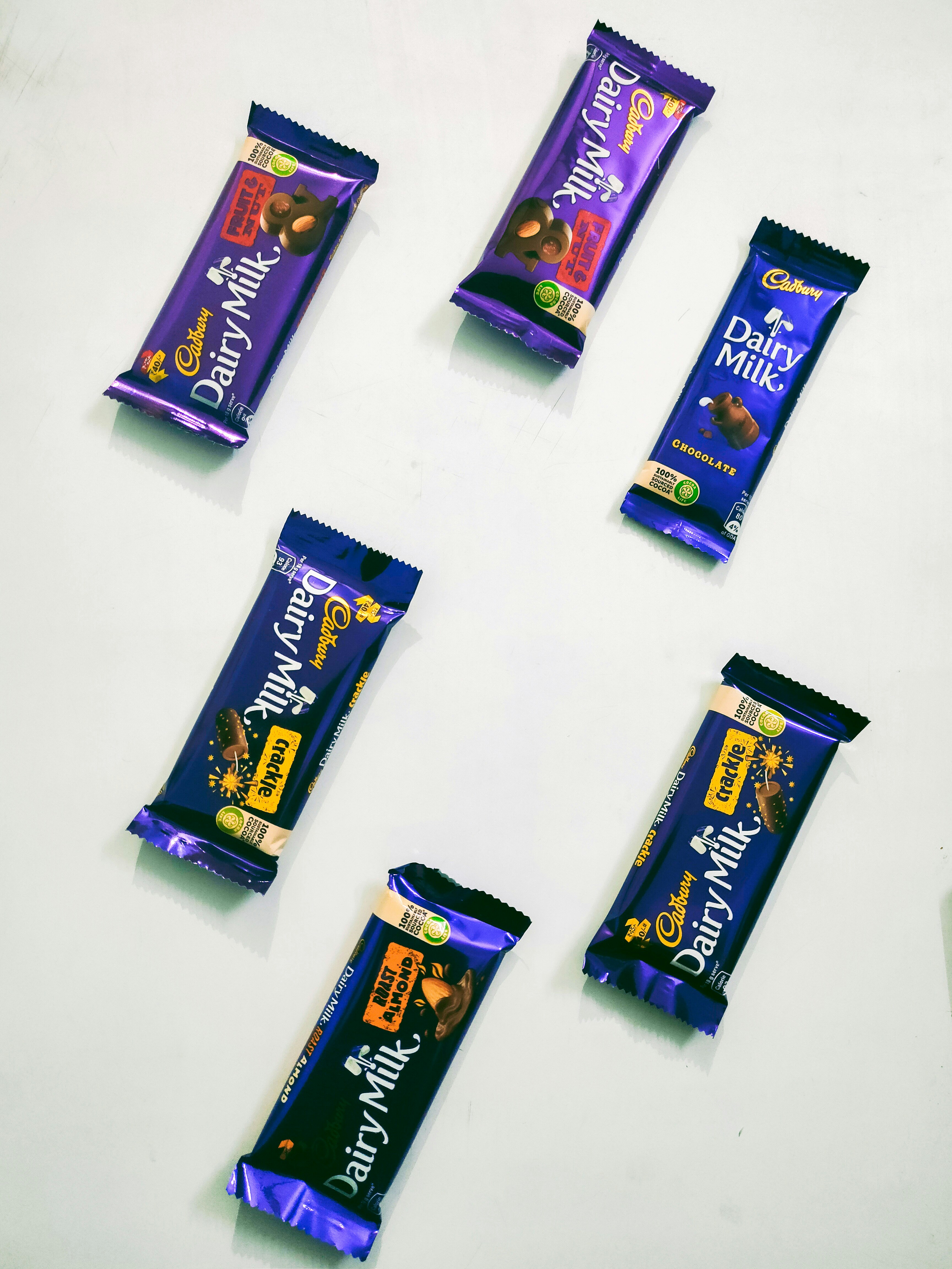 Six Cadbury Dairy Milk chocolate bars in various flavors and sizes on a white surface.