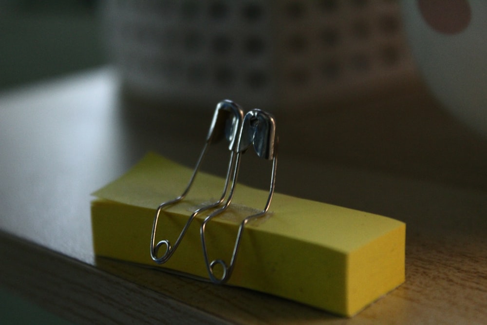 a pair of metal clips sitting on top of a yellow piece of paper