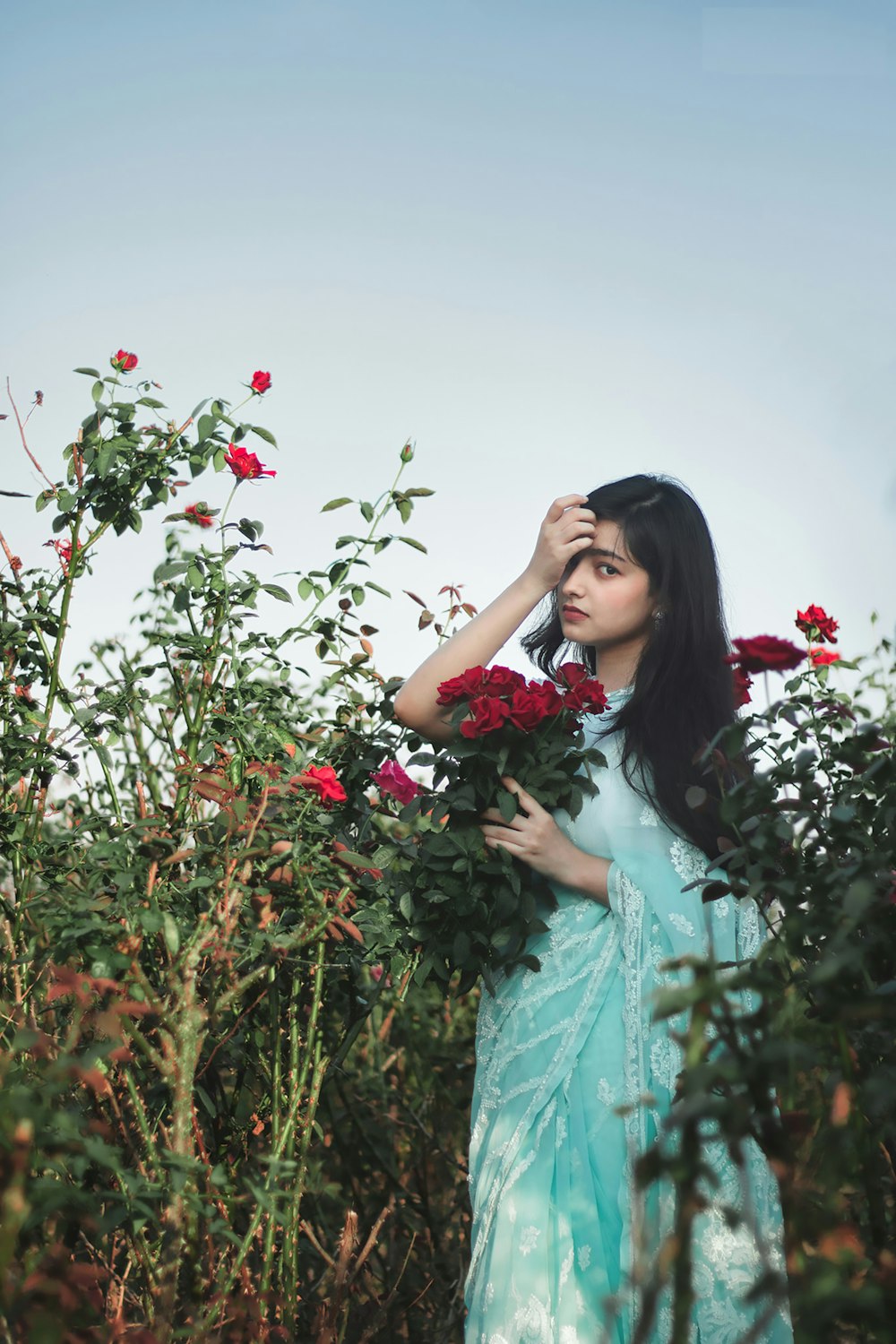 a woman in a blue dress standing in a field of roses