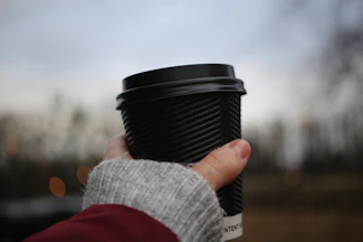 A close-up of a man wearing bright red gloves holding a coffee cup outside on a chilly day