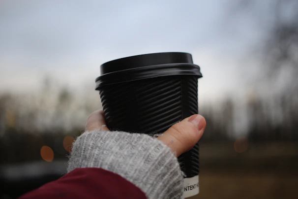 A close-up of a man wearing bright red gloves holding a coffee cup outside on a chilly day