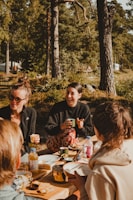 An outdoor urban scene featuring a group of Black friends sharing food and laughter around a picnic table.