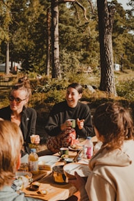 A group of friends relaxing on various styles of Campease chairs around a picnic table in the woods.