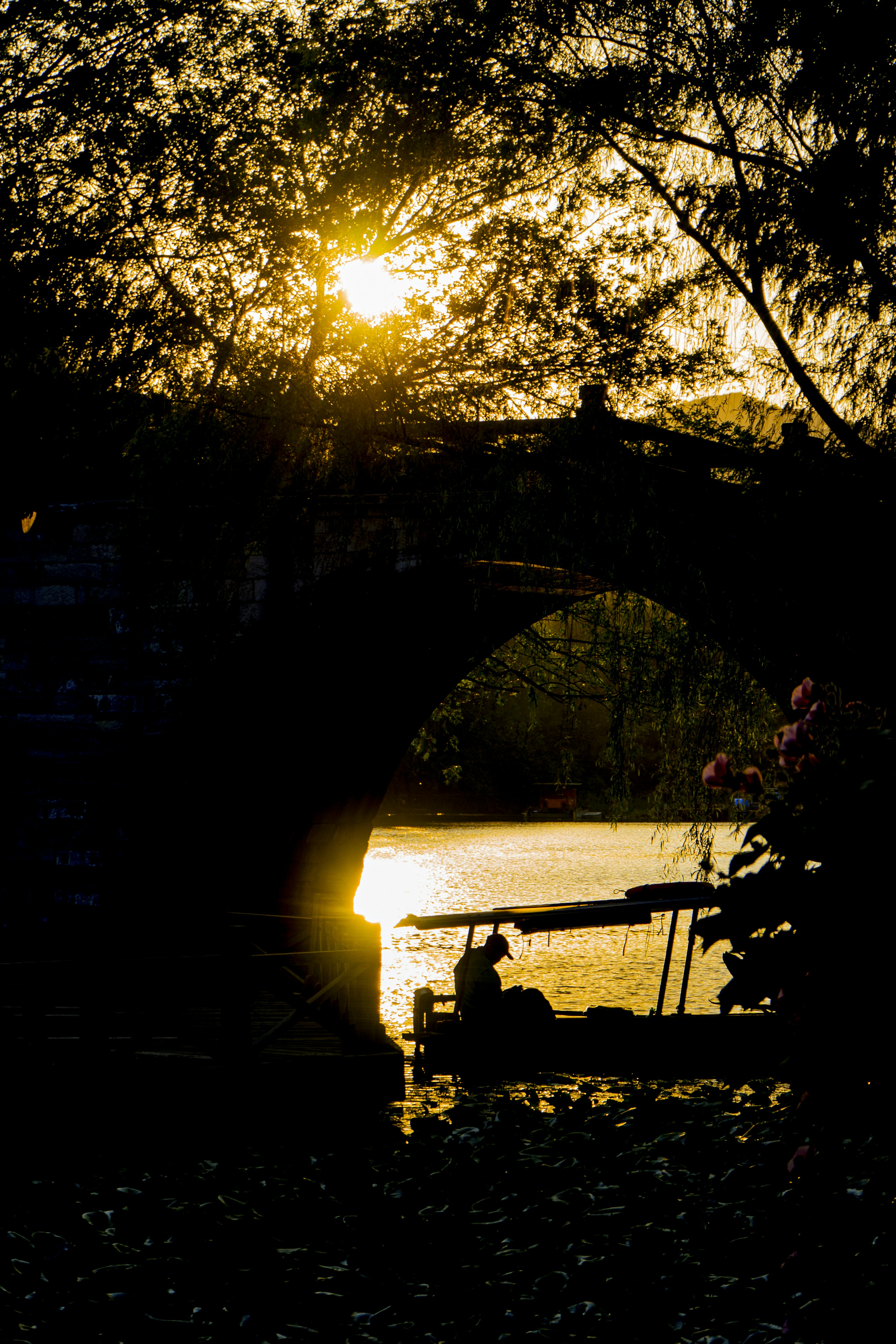 a boat traveling under a bridge at sunset