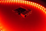 A close-up view of a computer motherboard or circuit board surrounded by a circular array of bright red LED lights, casting an intense glow over the surface.