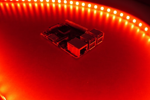 A close-up view of a computer motherboard or circuit board surrounded by a circular array of bright red LED lights, casting an intense glow over the surface.