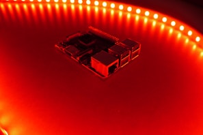 Close-up of a custom circuit board glowing with LED lights inside a sleek music synthesizer.