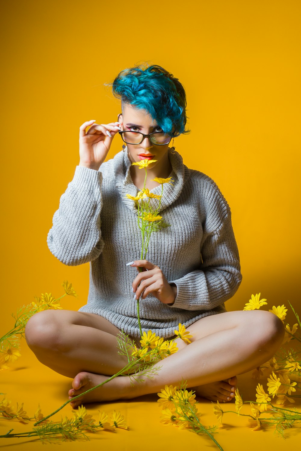 a woman with blue hair and glasses sitting on the ground