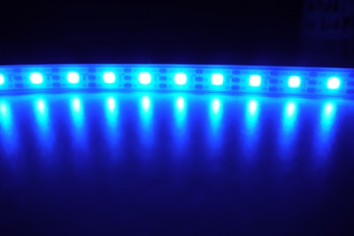 A series of bright blue LED lights arranged in a linear strip against a dark background, reflecting off a shiny surface and creating a glowing effect.