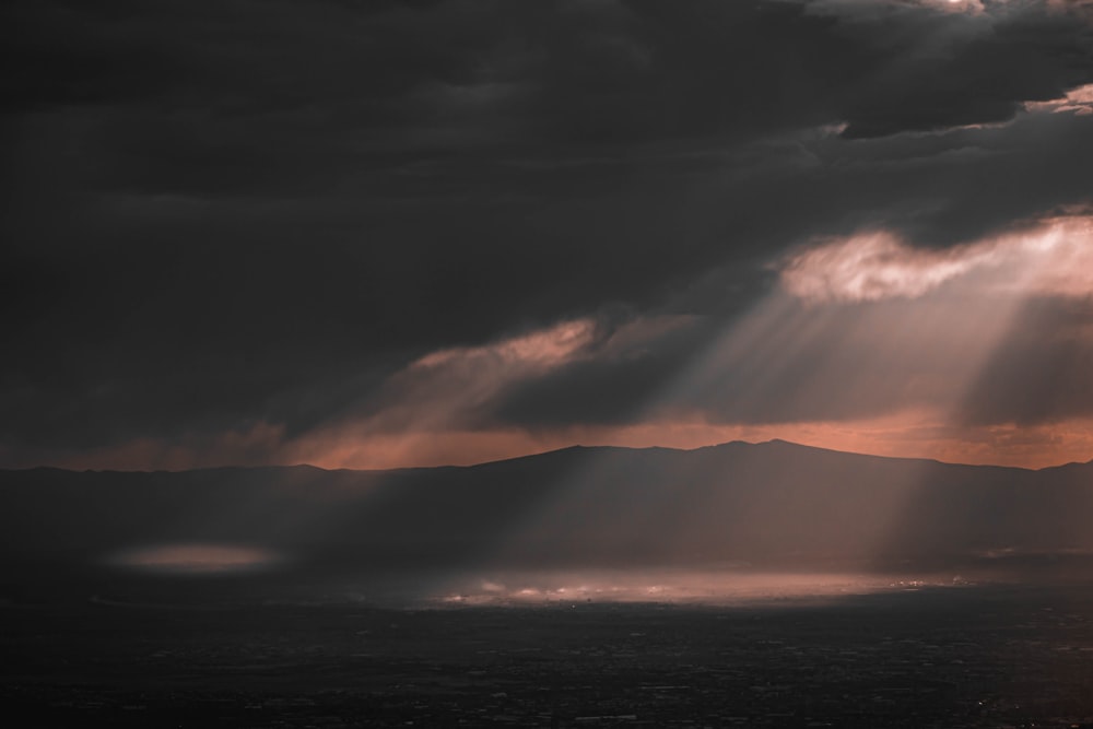 the sun shines through dark clouds over a mountain range