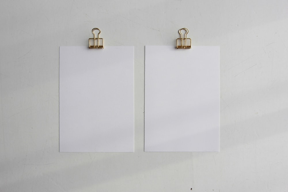 two blank paper with clippings attached to a wall