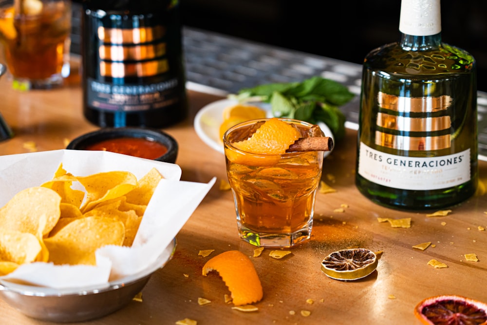 a wooden table topped with a bowl of chips and a bottle of wine