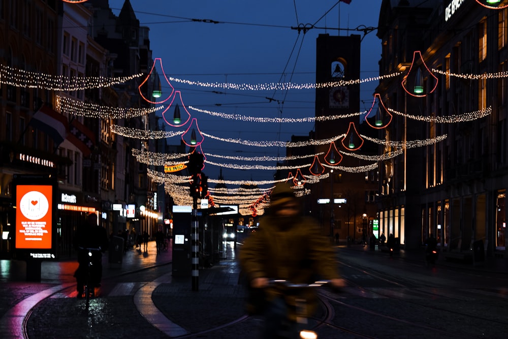 a man riding a bike down a street covered in christmas lights