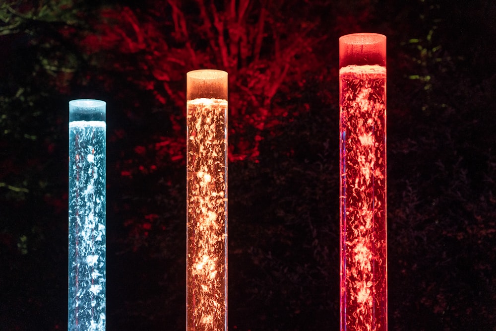 Tres luces de diferentes colores en la oscuridad con árboles en el fondo